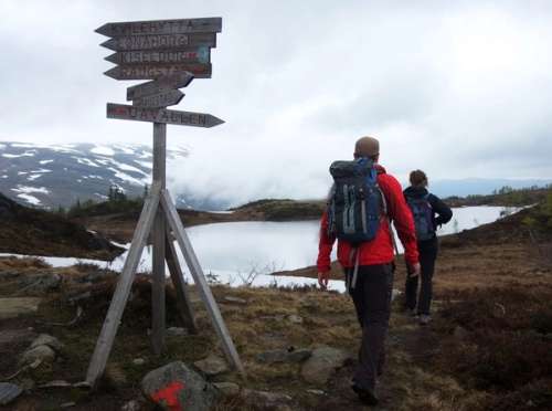 Two people walking past a sign in the mountains