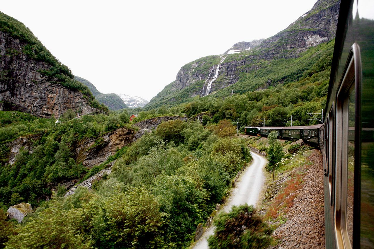 View from the window on the Flåm Railway where you see the train, a waterfall and lush mountain scenery