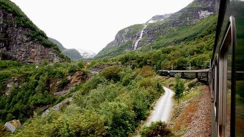 View from the window on the Flåm Railway where you see the train, a waterfall and lush mountain scenery