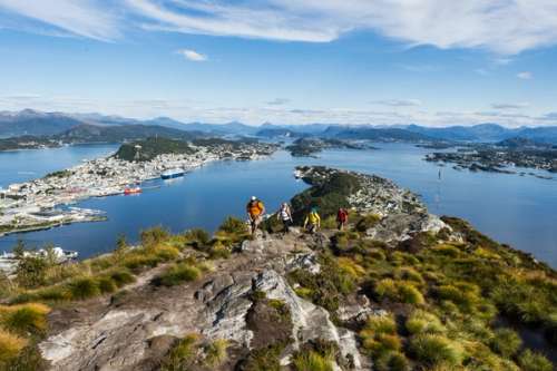 People walking up a mountain with a blue fjord in the background.