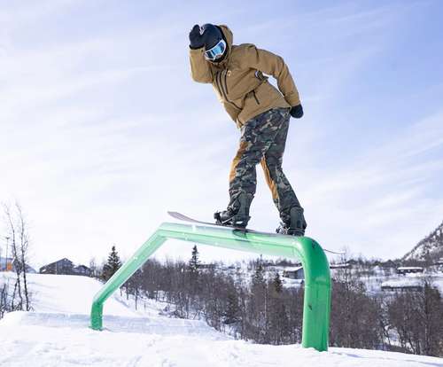 Person stands on a snowboard over a rail.