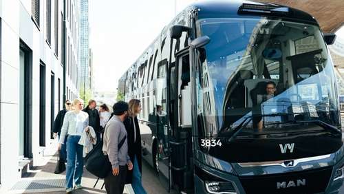 A Vy bus parked outside a white building, and a group of people on their way on board.