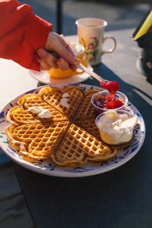Delicious heart-shaped waffle with sour cream and jam outside in the sun.