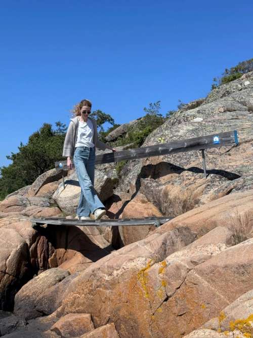 A small bridge between two rocks. The bridge features blue signage and there is a woman crossing it.