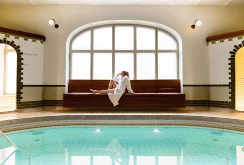 Woman sits on a bench by an indoor pool.