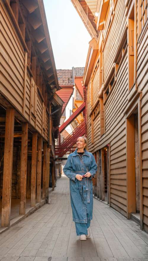 Woman walking through a narrow street with wooden buildings.