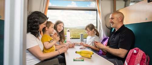 Innsiden av en kupé med en familie to voksne og tre barn som spiller kort ved et bord.