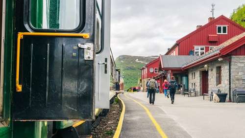Tog som står på en stasjon med rød bygning.