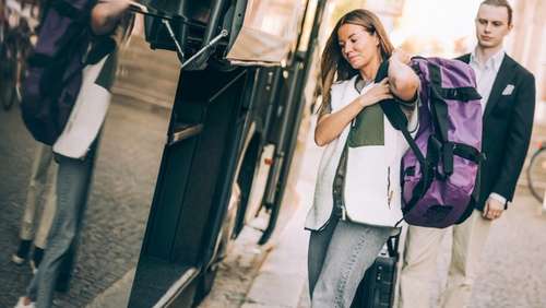 To people with luggage walking alongside a bus.
