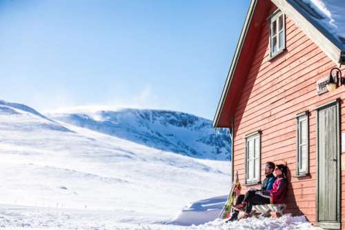 A couple sitting in the sun with their skis beside them, enjoying the mountain view.