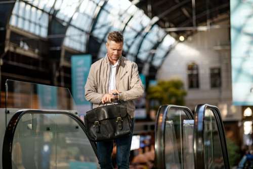 Mann står ved rulletrapp på en togstasjon og ser på klokken sin