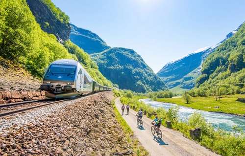 Tog som kjører ved siden av en vei med folk som sykler og går gjennom norsk landskap.