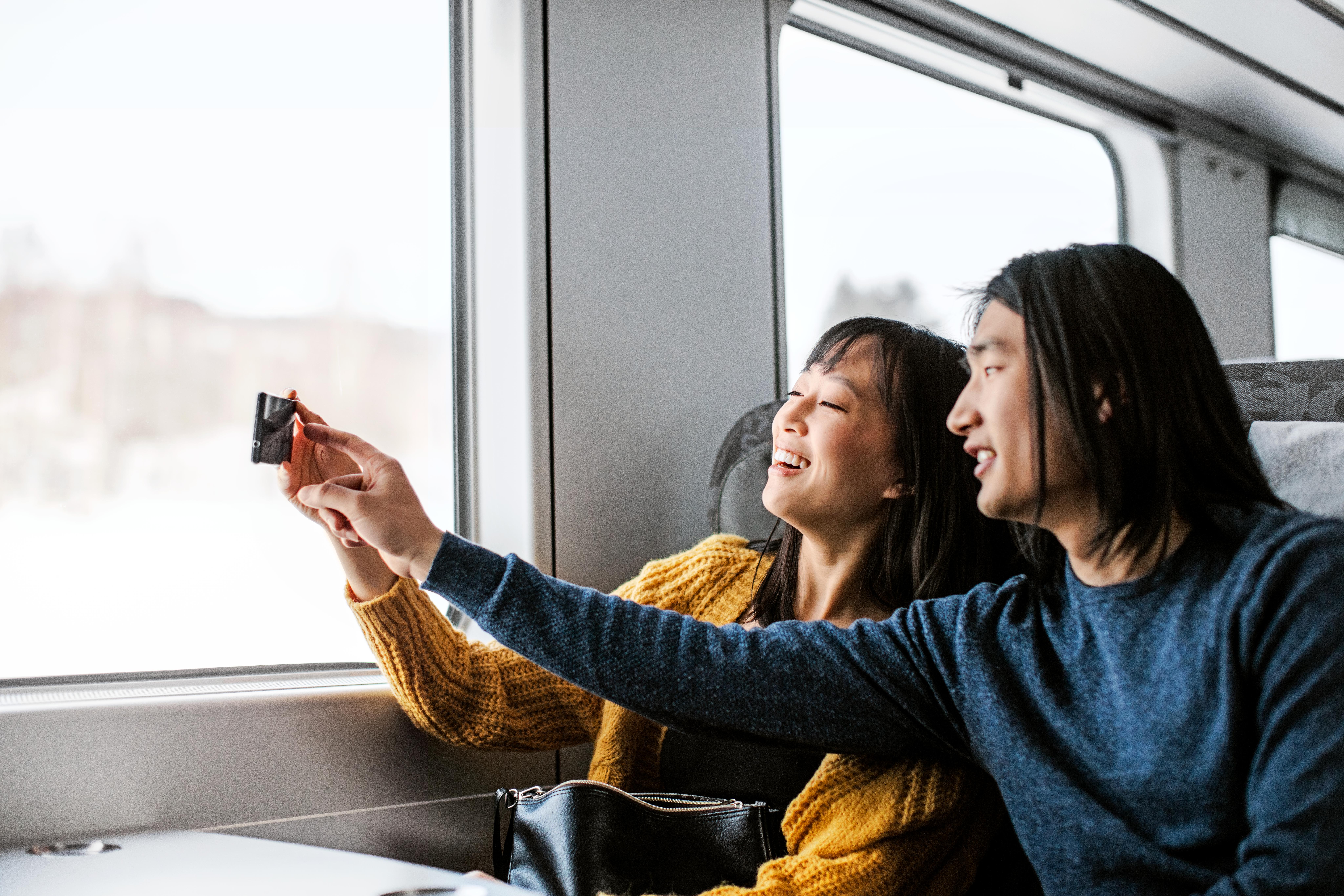 Two people on the train smiling and taking a picture out of the window.
