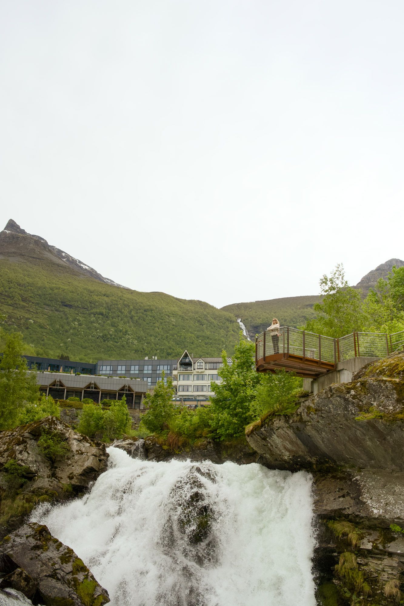 Foss og utkikkspunkt i Geiranger med fjell i bakgrunnen.