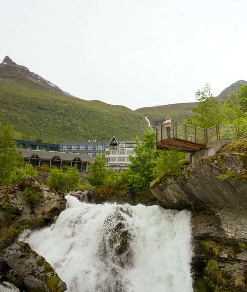 Foss og utkikkspunkt i Geiranger med fjell i bakgrunnen.
