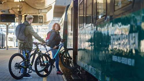 A woman and man smile as they board the train to Bergen, each carrying their own bicycle.