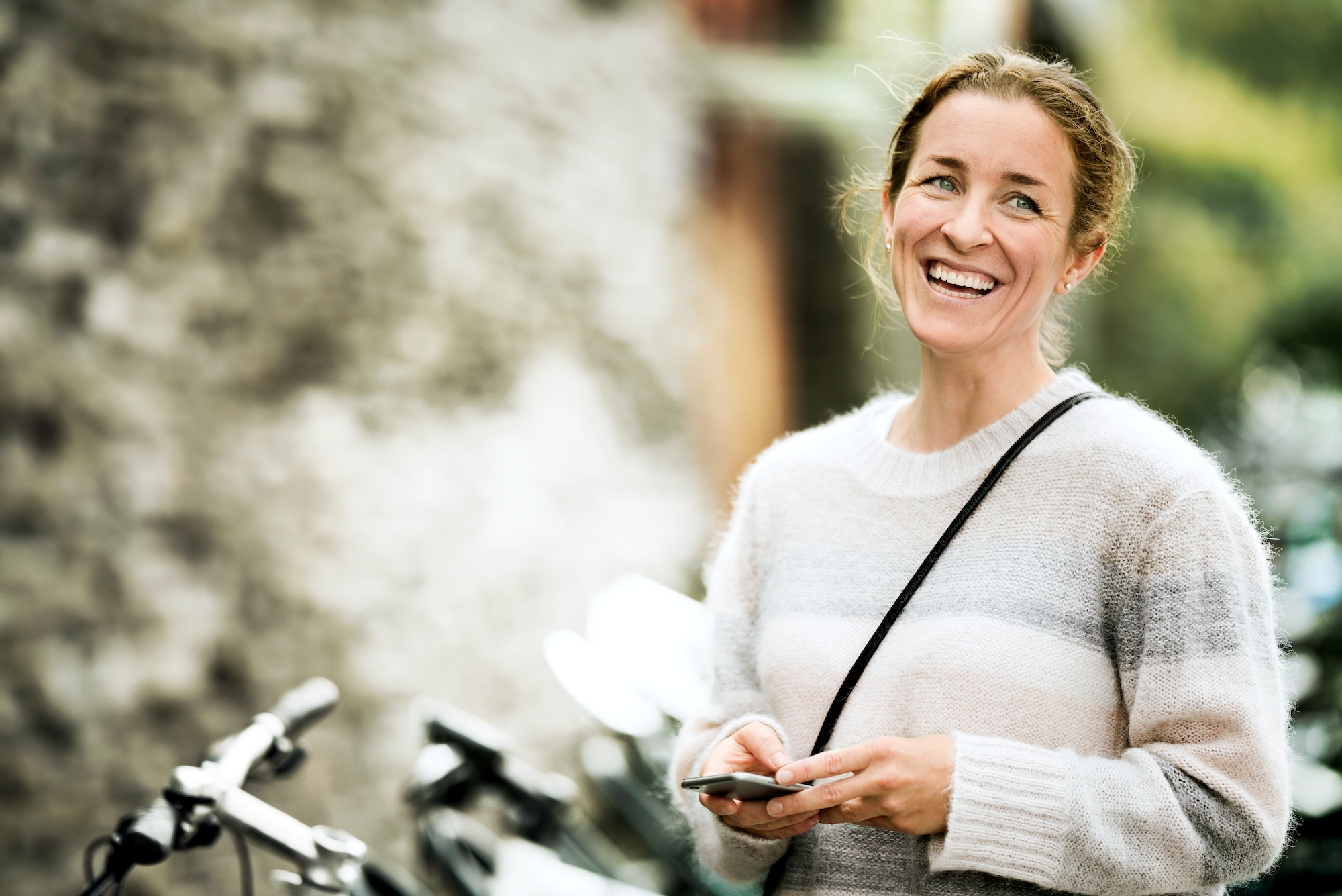 Woman holding a mobile phone, standing next to a bike.