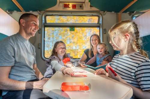 Father, mother and three children playing cards in a train compartment.