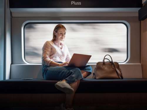Kvinne sitter med laptop ved vinduet på Pluss på Bergensbanen