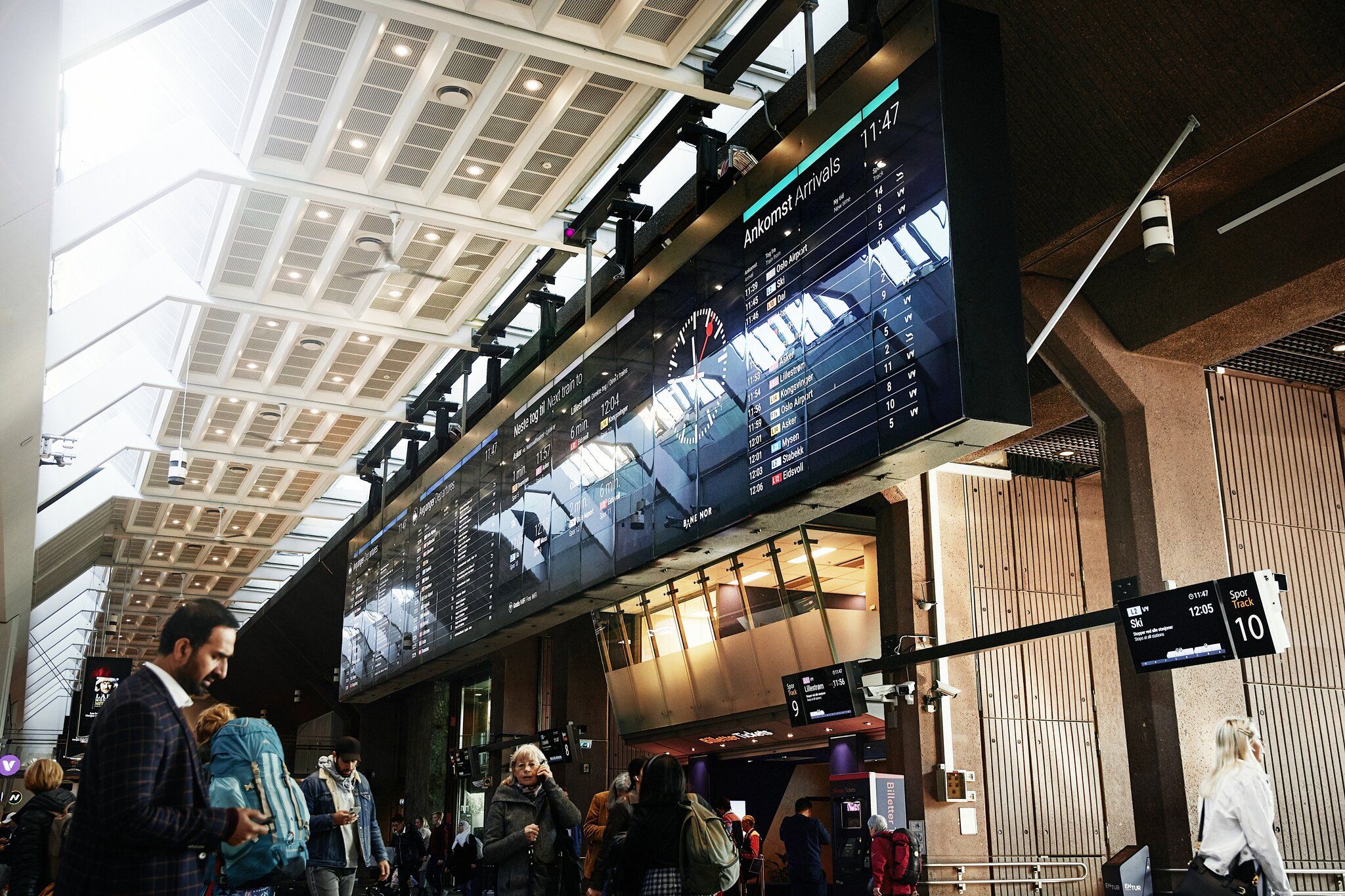 Avgangshallen på Oslo S med tavle med avgang- og ankomsttider og mennersker i bevegelse.