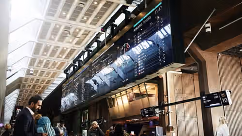 Avgangshallen på Oslo S med tavle med avgang- og ankomsttider og mennersker i bevegelse.