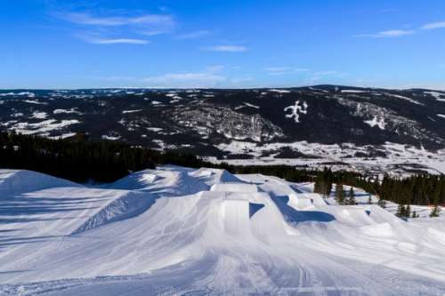 Hvite skibakker med hopp med blå himmel og fjell i bakgrunnen.