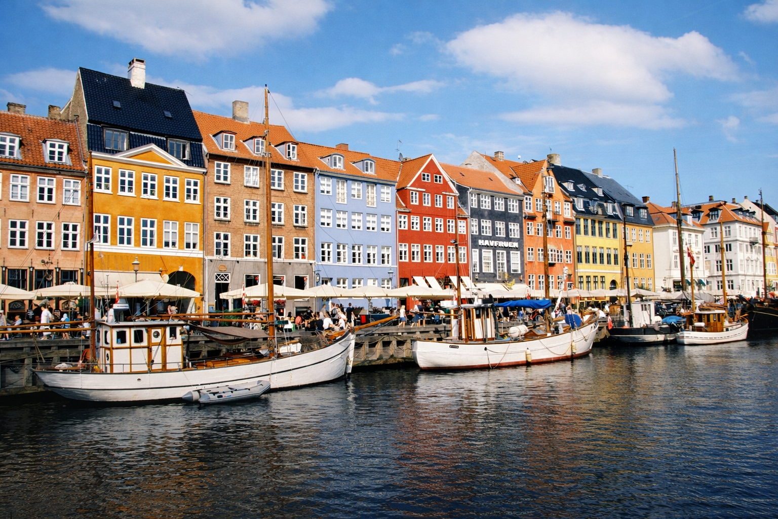 Båter som ligger foran fargerike hus i Nyhavn i København