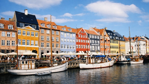 Båter som ligger foran fargerike hus i Nyhavn i København