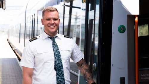 Train driver Kenneth stands outside a train and smiles