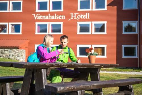 To personer sitter på en benk og spiser foran Vatnahalsen hotell
