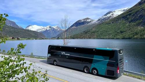 View of a double-decker bus in a bus shelter by a fjord with mountains in the background