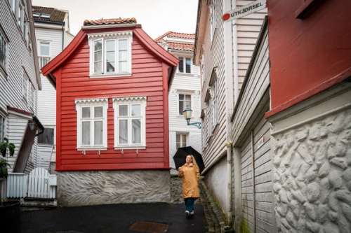 Woman with an umbrella and yellow raincoat walking between old wooden buildings.