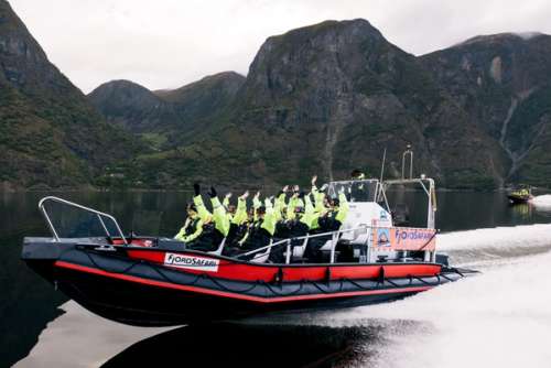 Mennesker i en svart og rød RIB båt som kjører over en fjord.