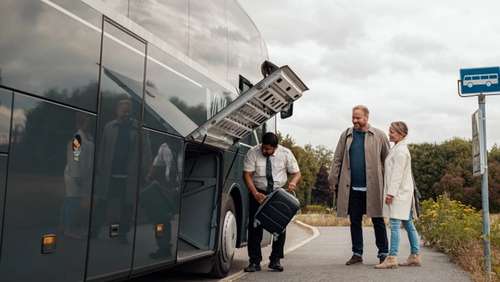 The bus driver is helping to put luggage in the luggage compartment of the bus.