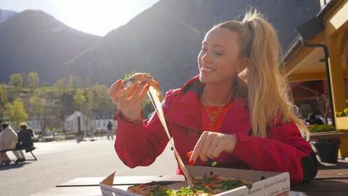 Smilende kvinne som holder et pizzastykke
