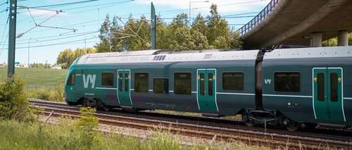 Green train passing under a bridge.
