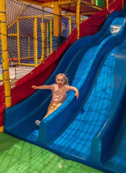 A small girl sliding down a blue slide.