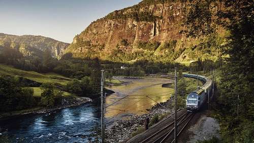 Train driving through the mountain landscape alongside a river.