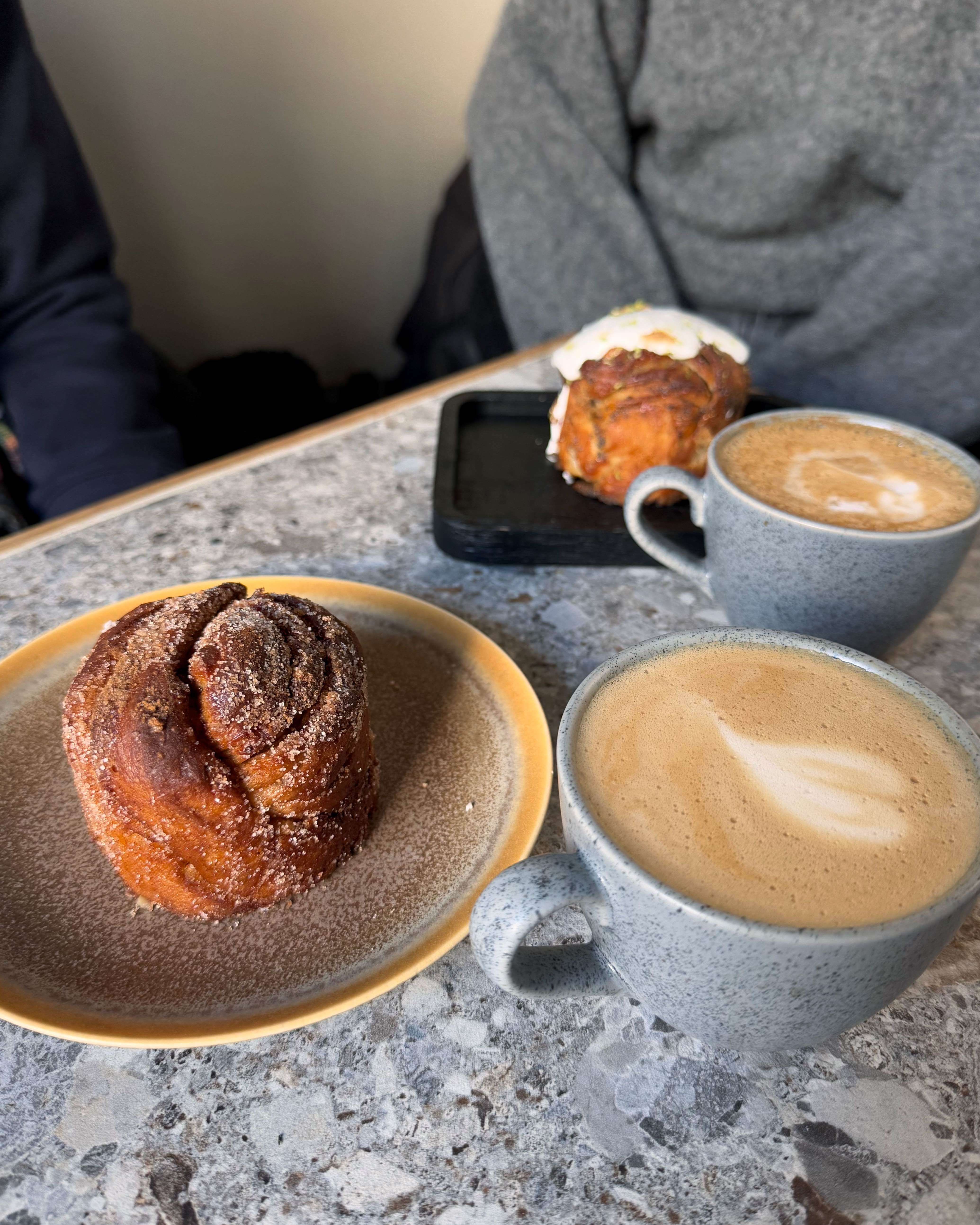 En tallerken med kanelbolle med sukker på og to kopper med kaffe.