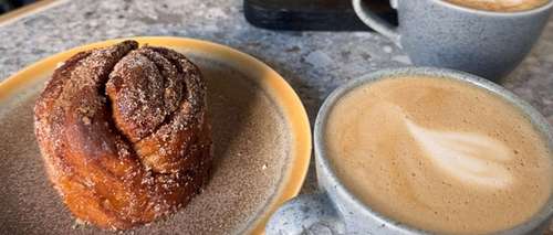 En tallerken med kanelbolle med sukker på og to kopper med kaffe.