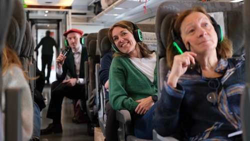 People sitting on the train with headphones on, listening to an audio guide.
