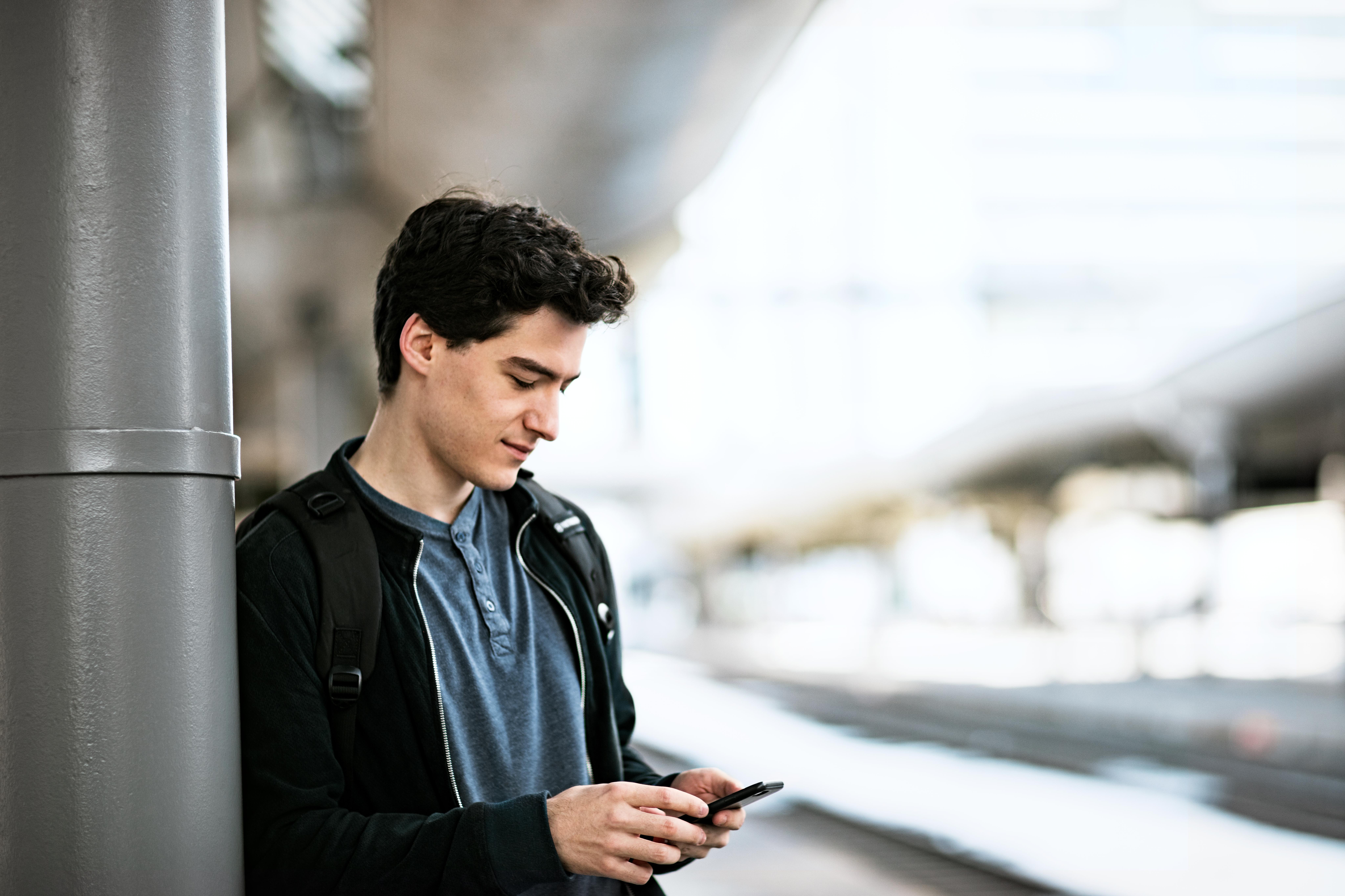 A young man looks at his mobile phone while waiting for a train on the platform