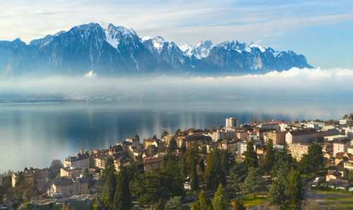 Byen Montreux i forgrunnen, med enn innsjø og snødekte fjell i bakgrunnen.