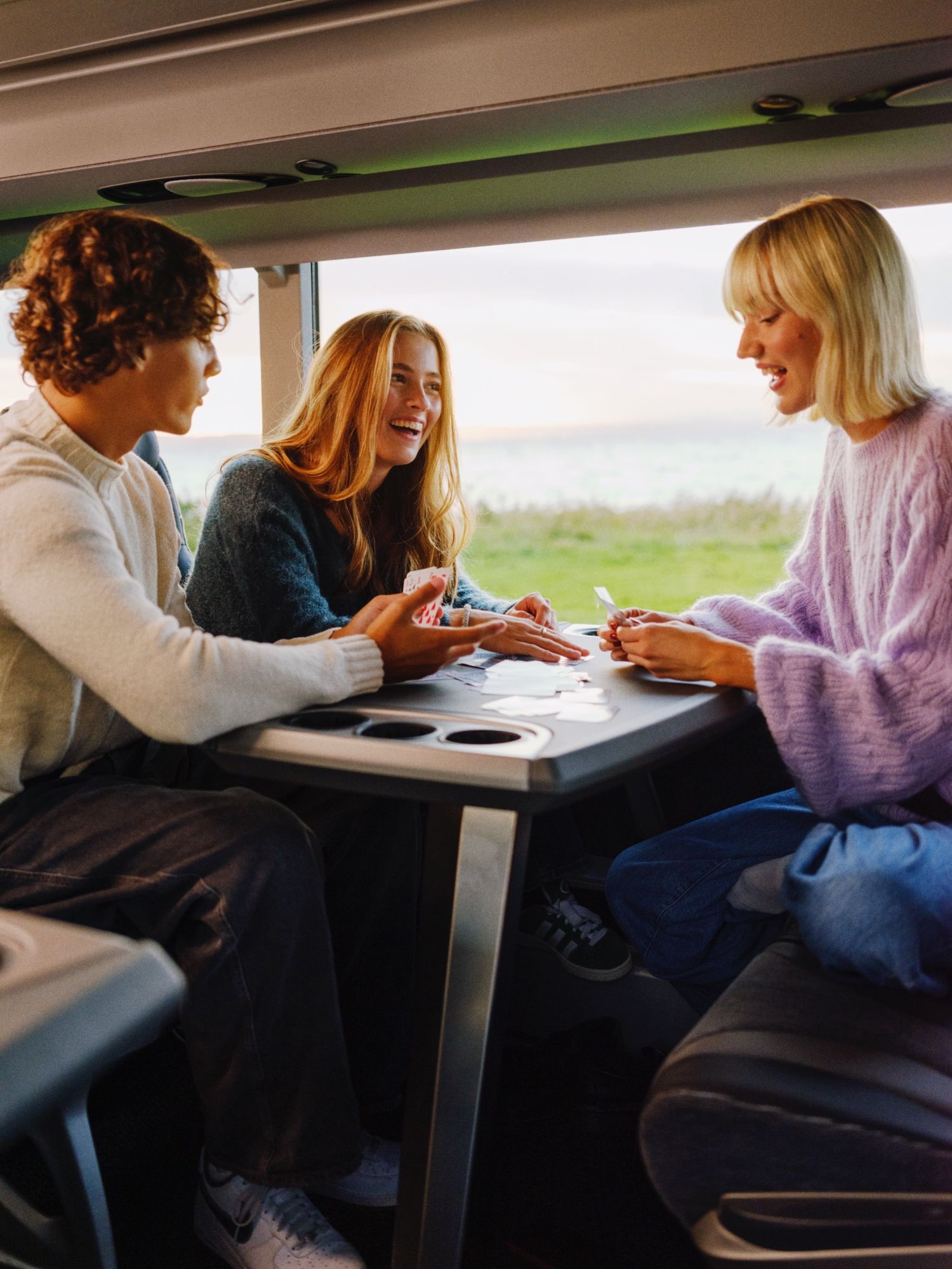 To unge kvinner og ein ung mann spelar kort på bussen.