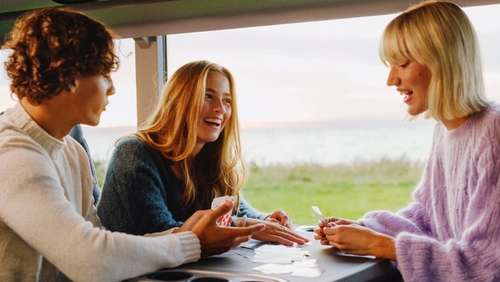 Two young women and a young man are playing cards on the bus.