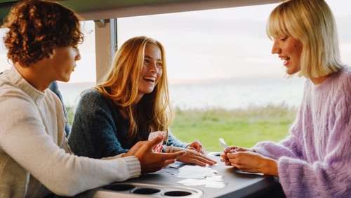 To unge kvinner og ein ung mann spelar kort på bussen.