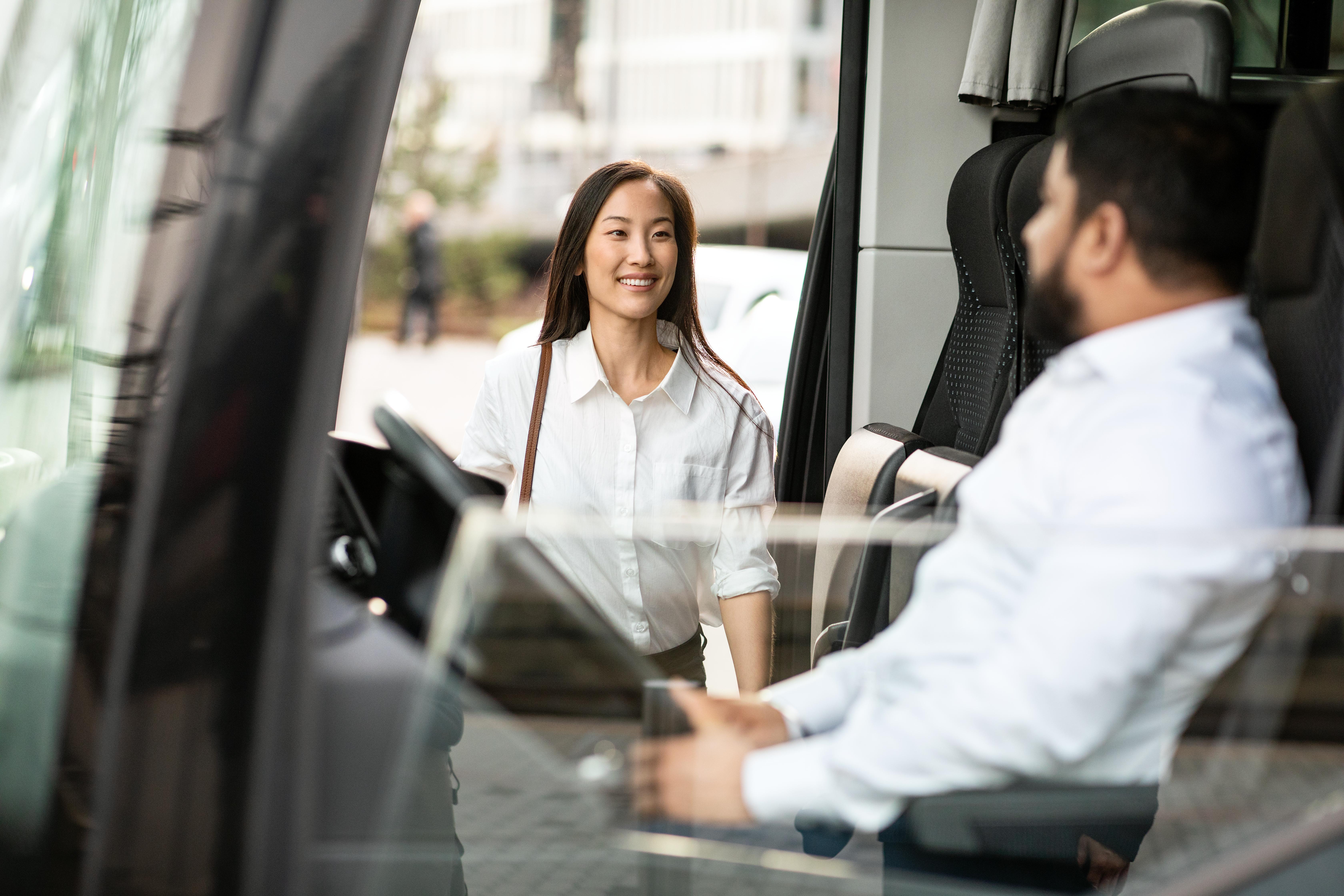 Female passenger boards the bus and smiles at the driver