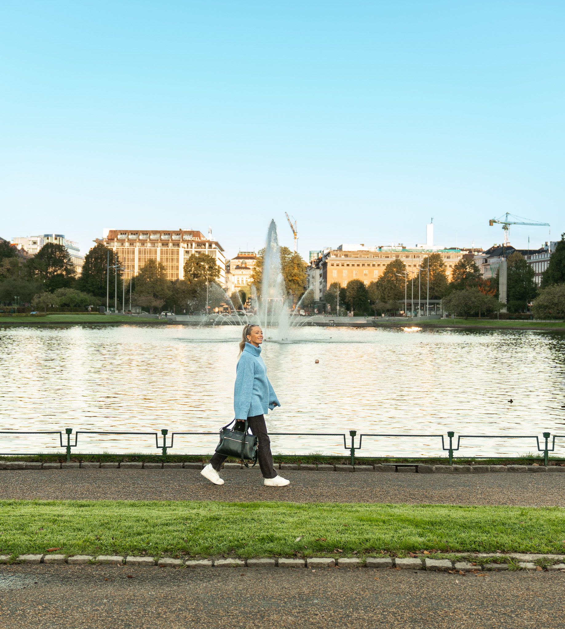 A woman with a blue sweater walking along a pond in Bergen.