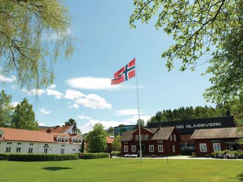 Several houses surrounding a Norwegian flag at Hadeland Glassverk.