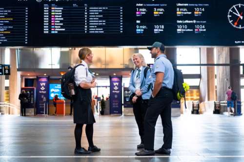 Tre personer prater sammen foran en avgangstavle på togstasjonen.